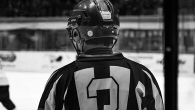 Black and white photo of ice hockey player in helmet from behind, captured during a match.