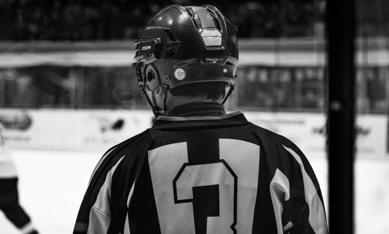 Black and white photo of ice hockey player in helmet from behind, captured during a match.