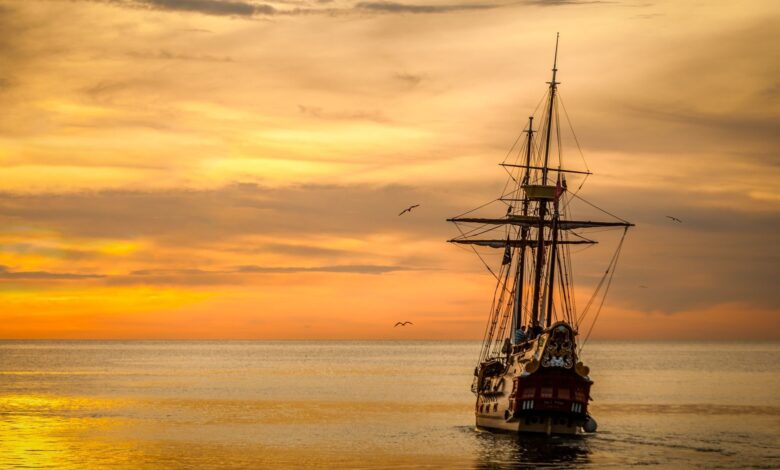 A majestic pirate ship sails into the serene waters at sunset, casting a dramatic silhouette.