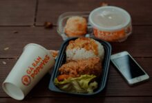 Delicious fried chicken meal from Popeyes with accompanying smartphone and drink on wooden table.
