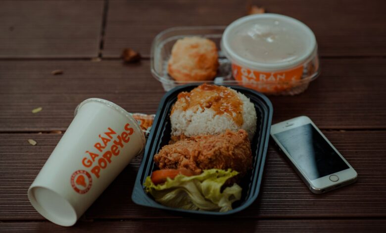 Delicious fried chicken meal from Popeyes with accompanying smartphone and drink on wooden table.