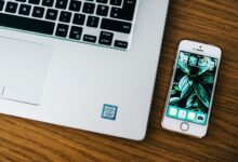 Close-up of a laptop and smartphone on a wooden desk in an office setting.