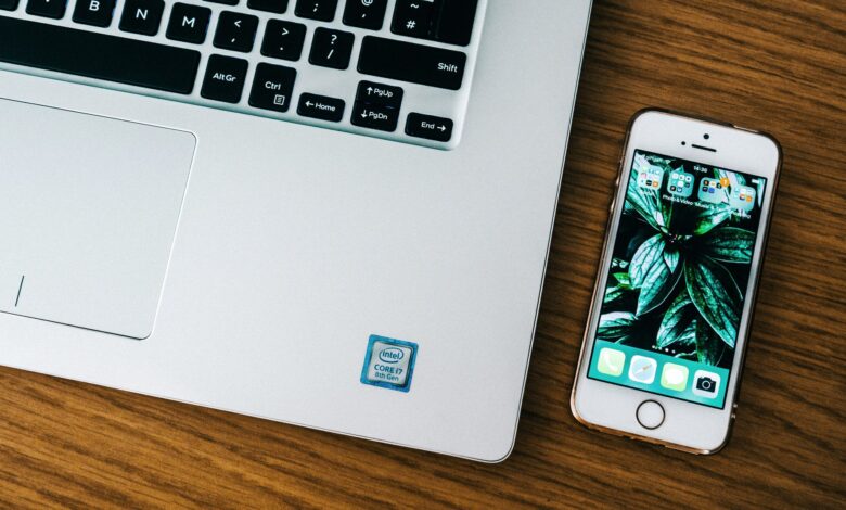 Close-up of a laptop and smartphone on a wooden desk in an office setting.