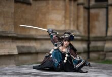 Female performer in traditional samurai costume poses with sword outdoors.
