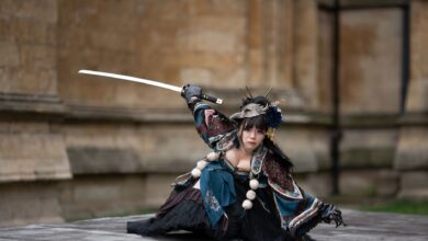 Female performer in traditional samurai costume poses with sword outdoors.