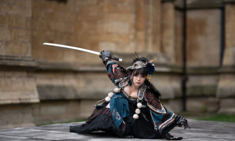 Female performer in traditional samurai costume poses with sword outdoors.
