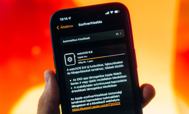 Hand holding a smartphone displaying WatchOS 8.6 update notification against warm gradient background.