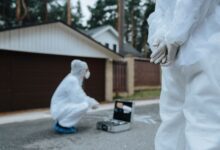 Forensic investigators in white suits and masks examining a crime scene outside a residential area.
