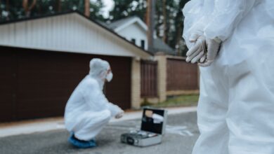 Forensic investigators in white suits and masks examining a crime scene outside a residential area.