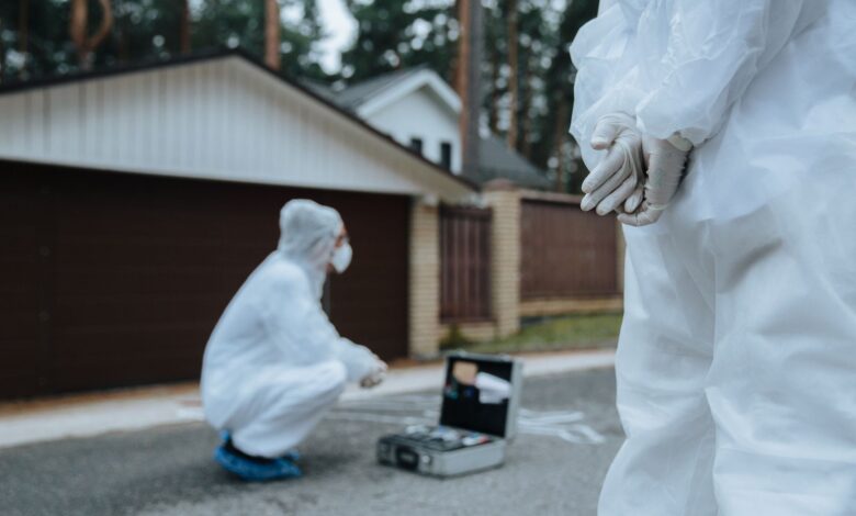 Forensic investigators in white suits and masks examining a crime scene outside a residential area.