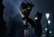 A man in dark clothing holds a pocket watch on a dimly lit street at night.