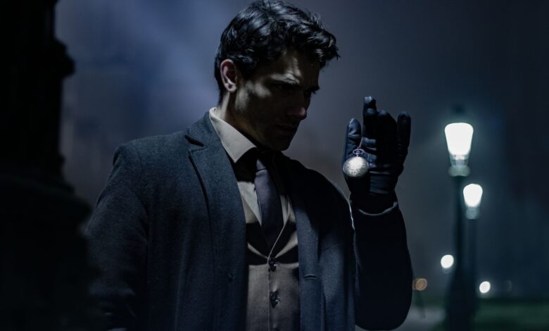 A man in dark clothing holds a pocket watch on a dimly lit street at night.