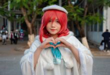 Portrait of a woman in cosplay with red hair, heart gesture outdoors.
