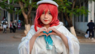 Portrait of a woman in cosplay with red hair, heart gesture outdoors.