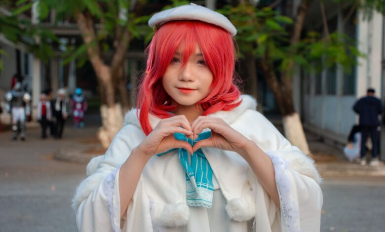 Portrait of a woman in cosplay with red hair, heart gesture outdoors.