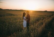 A loving couple stands embrace in a scenic wheat field during sunset, capturing romance.