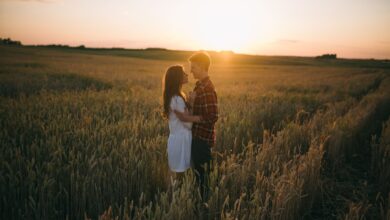 A loving couple stands embrace in a scenic wheat field during sunset, capturing romance.