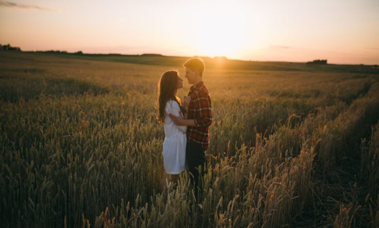 A loving couple stands embrace in a scenic wheat field during sunset, capturing romance.