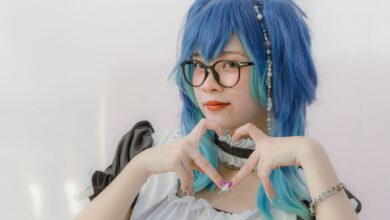 Creative cosplay portrait featuring a woman in costume with blue hair and glasses, forming a heart gesture.