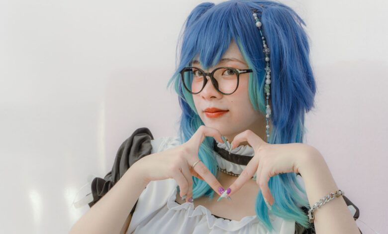 Creative cosplay portrait featuring a woman in costume with blue hair and glasses, forming a heart gesture.