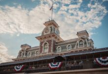 Iconic entrance to Walt Disney World Railroad at Magic Kingdom, Orlando, Florida, with vintage architecture and American flags.