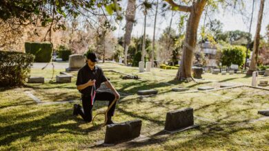 A man kneeling with a memento in a tranquil cemetery surrounded by tombstones and trees.