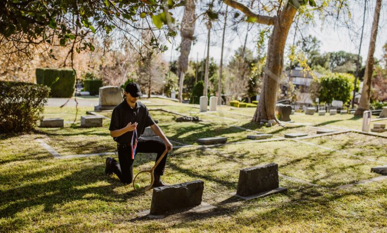 A man kneeling with a memento in a tranquil cemetery surrounded by tombstones and trees.