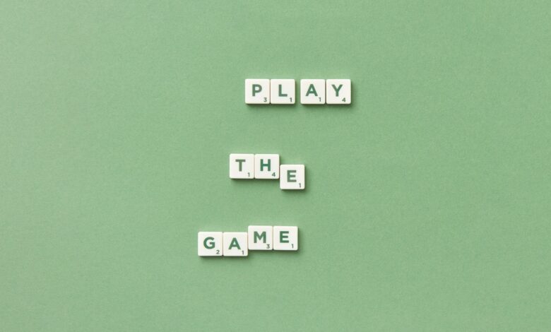 Scrabble letter tiles spelling 'Play the Game' on light green background.