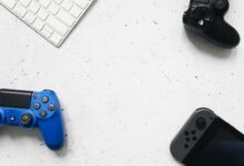 A variety of game controllers and a keyboard arranged on a white textured surface, offering a minimalist gaming setup.
