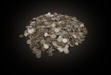 A large pile of assorted coins on a dark black background, symbolizing wealth and finance.