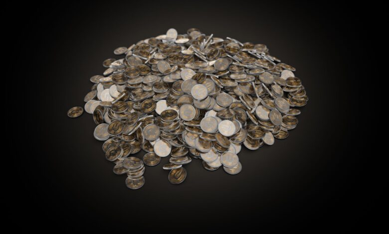 A large pile of assorted coins on a dark black background, symbolizing wealth and finance.