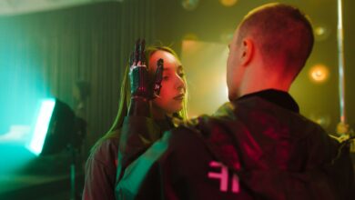 A man with a prosthetic hand gently touches a woman's face in a cyberpunk setting.