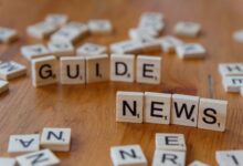 Close-up of Scrabble tiles spelling 'Guide' and 'News' on a wooden surface.