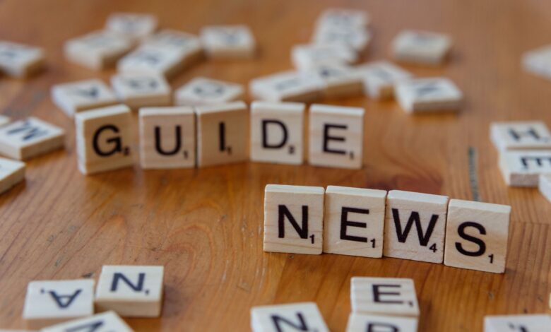 Close-up of Scrabble tiles spelling 'Guide' and 'News' on a wooden surface.