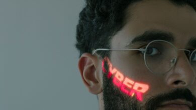 Close-up of a bearded man wearing eyeglasses with 'CYBER' text projected on his face.