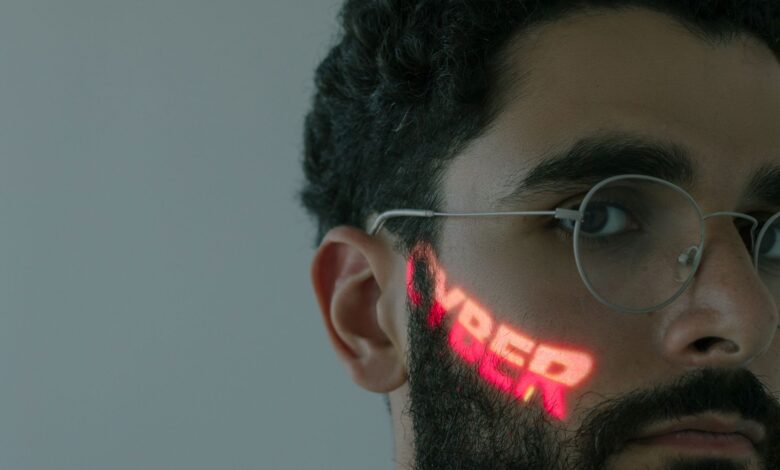 Close-up of a bearded man wearing eyeglasses with 'CYBER' text projected on his face.