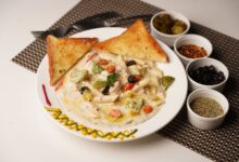 Delicious creamy pasta with toast served with olives, herbs, and peppers on a decorated plate.