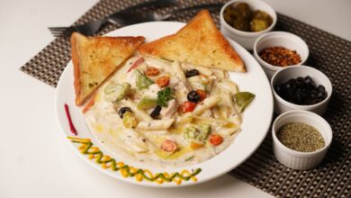 Delicious creamy pasta with toast served with olives, herbs, and peppers on a decorated plate.