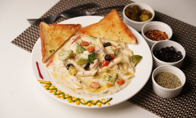 Delicious creamy pasta with toast served with olives, herbs, and peppers on a decorated plate.