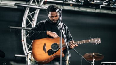 A male musician tuning his guitar on stage before a live performance.
