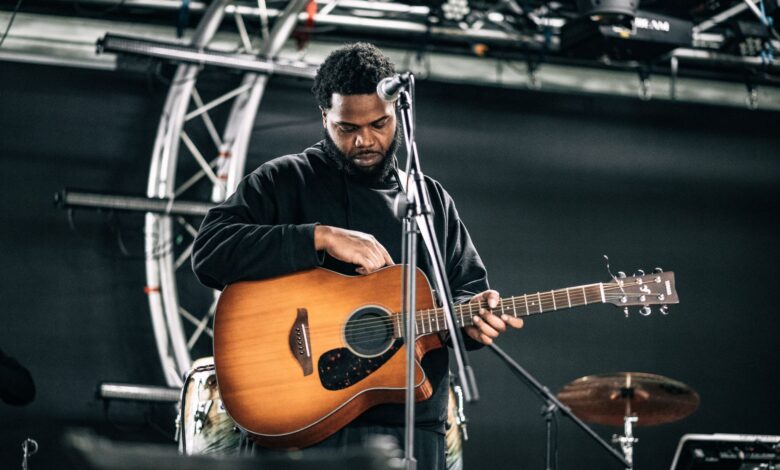 A male musician tuning his guitar on stage before a live performance.