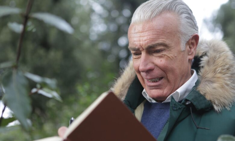 Elderly man in winter coat, writing in a notebook outdoors with a thoughtful expression.