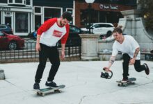 Two skateboarders enjoying a casual ride in a vibrant urban area, one holding a camera.