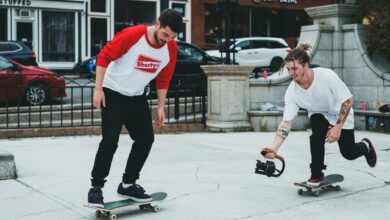 Two skateboarders enjoying a casual ride in a vibrant urban area, one holding a camera.