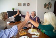 A group of senior friends enjoying dinner together, sharing a high five in a warm, friendly setting.