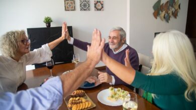 A group of senior friends enjoying dinner together, sharing a high five in a warm, friendly setting.
