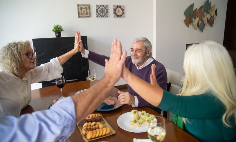 A group of senior friends enjoying dinner together, sharing a high five in a warm, friendly setting.