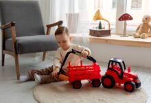 A young child playing with a red toy tractor indoors, surrounded by cozy decor.