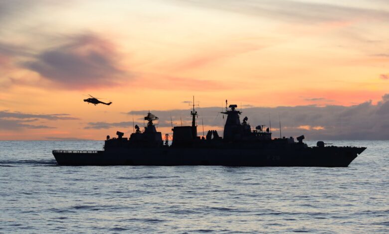 Silhouette of a warship and helicopter at sea during sunset.