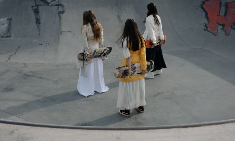 Three women skateboarders in stylish outfits strolling in a skatepark, holding skateboards.